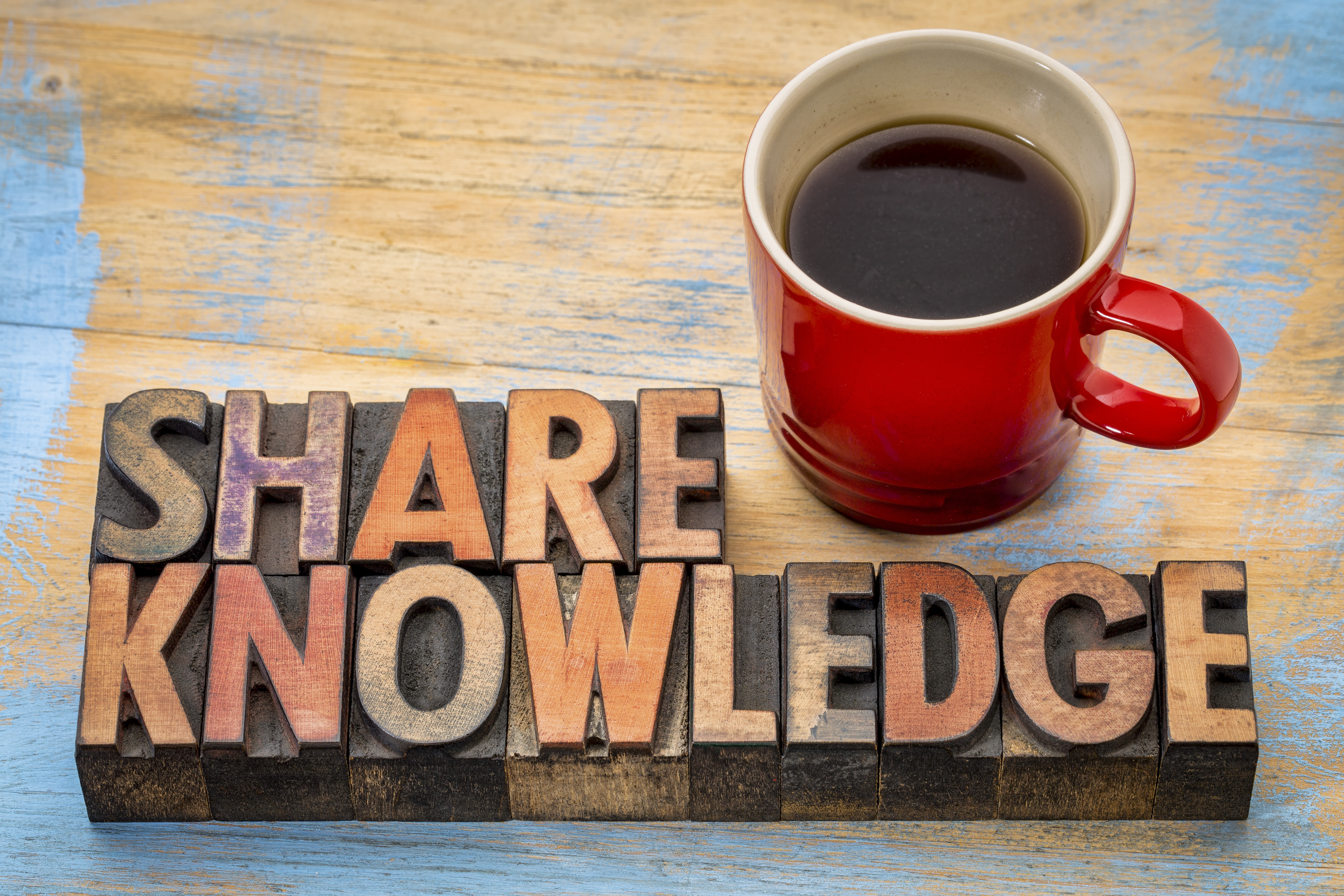 ナレッジシェアのイメージ画像。「SHARE KNOWLEDGE」と書かれた木製のピースとコーヒーの写真